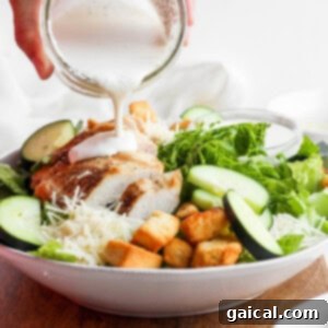 A hand pouring homemade Caesar dressing generously over a vibrant green salad, making it look incredibly appetizing.