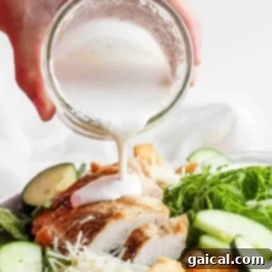 A person pouring a rich, creamy white dressing generously over a vibrant green salad, making it irresistible.