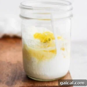 A mason jar carefully filled with all the liquid and creamy ingredients for a delicious Caesar dressing, perfectly poised for mixing.