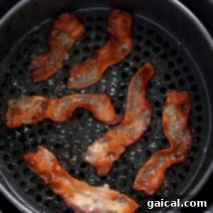 Bacon cooking in an air fryer basket, beginning to crisp.