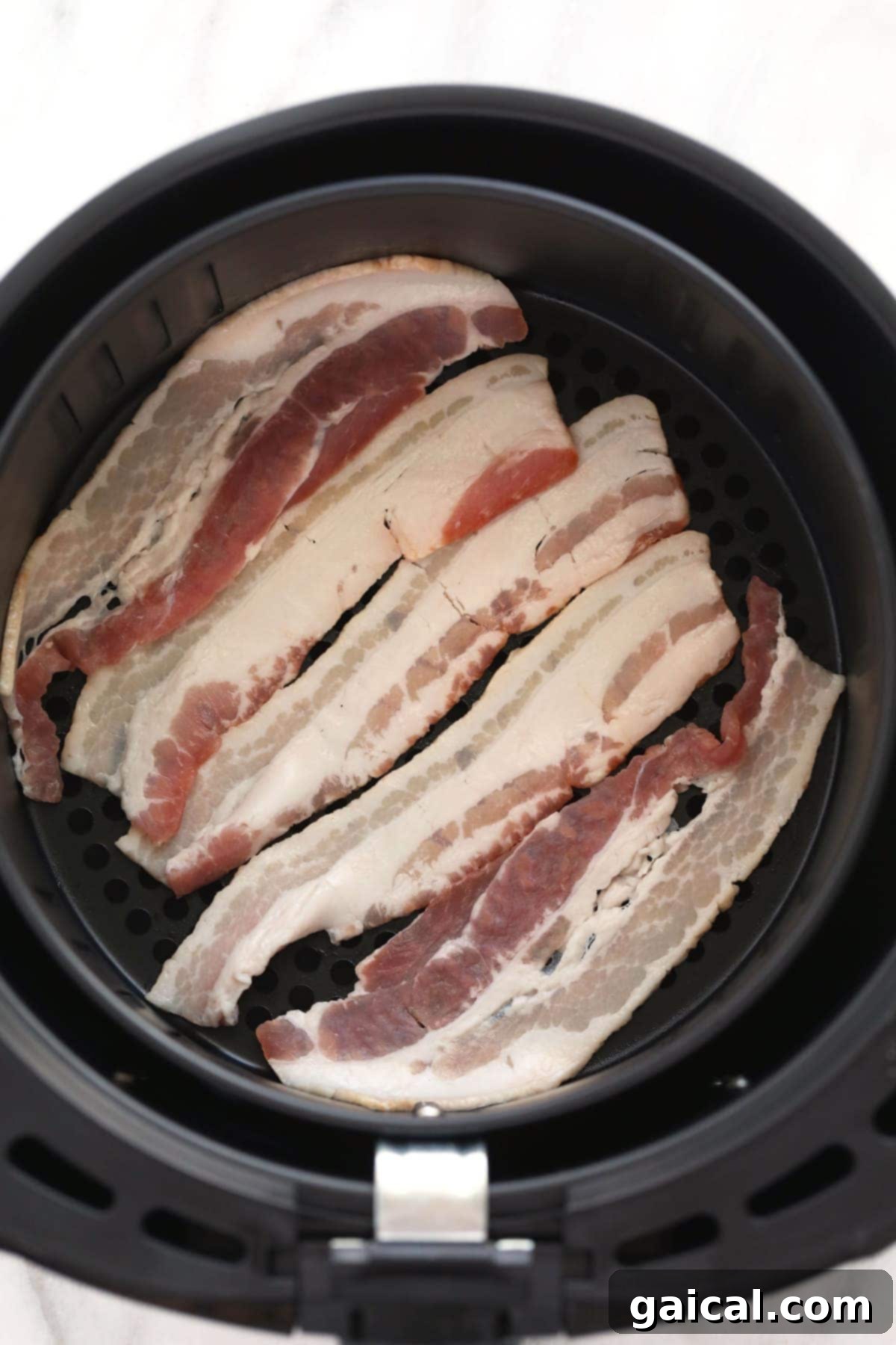 Uncooked bacon strips neatly arranged in a single layer inside an air fryer basket.