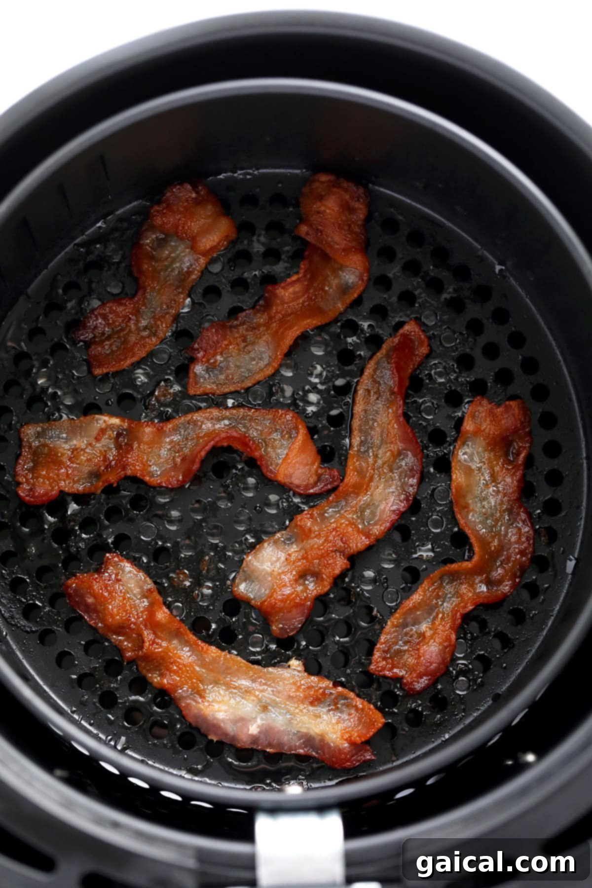 Crispy, perfectly cooked bacon strips in an air fryer basket after cooking.