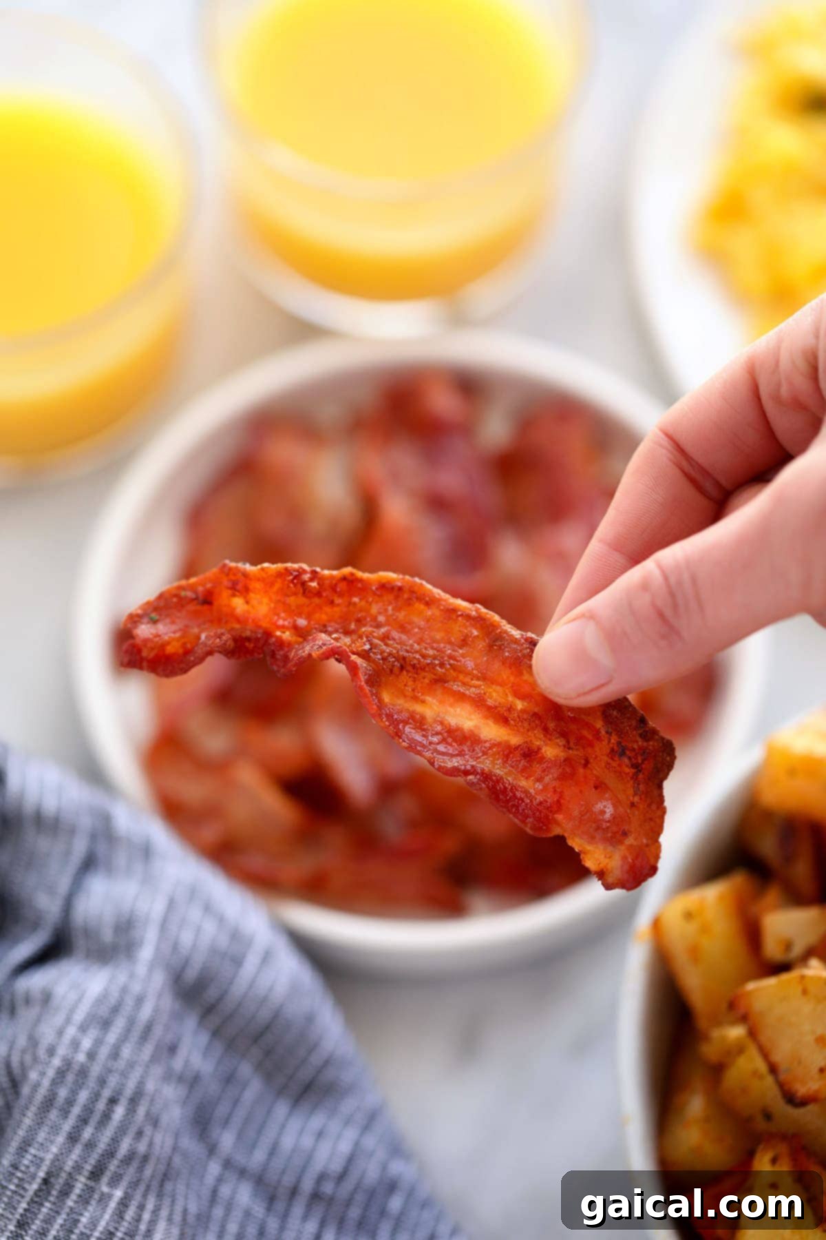 A hand holding a perfectly cooked, crispy strip of air fryer bacon.
