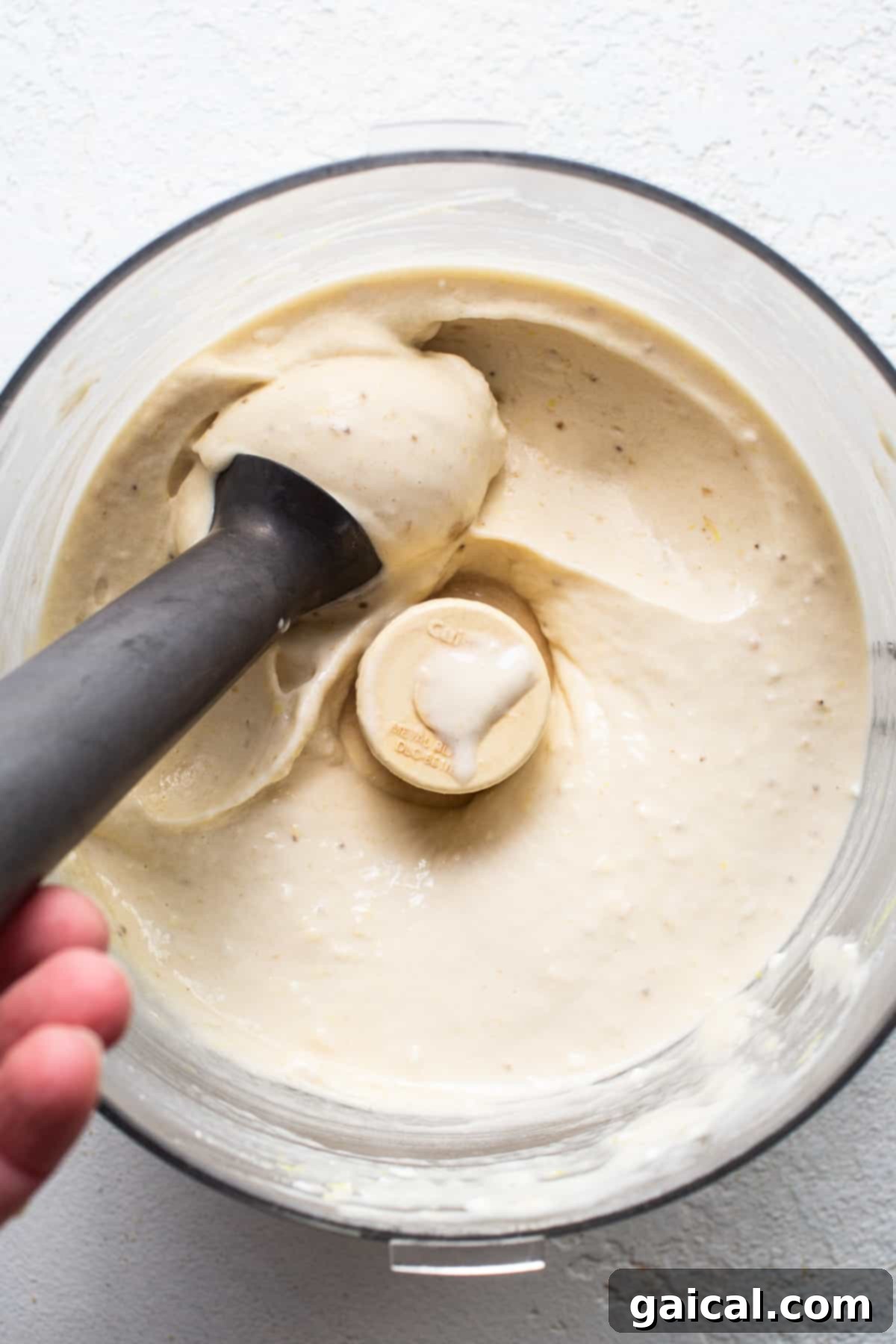 A hand holding a black handle in a bowl of white liquid, blending banana nice cream.