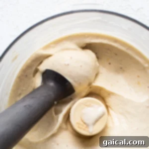 A blender filled with creamy banana nice cream, with a black tamper blending the mixture.