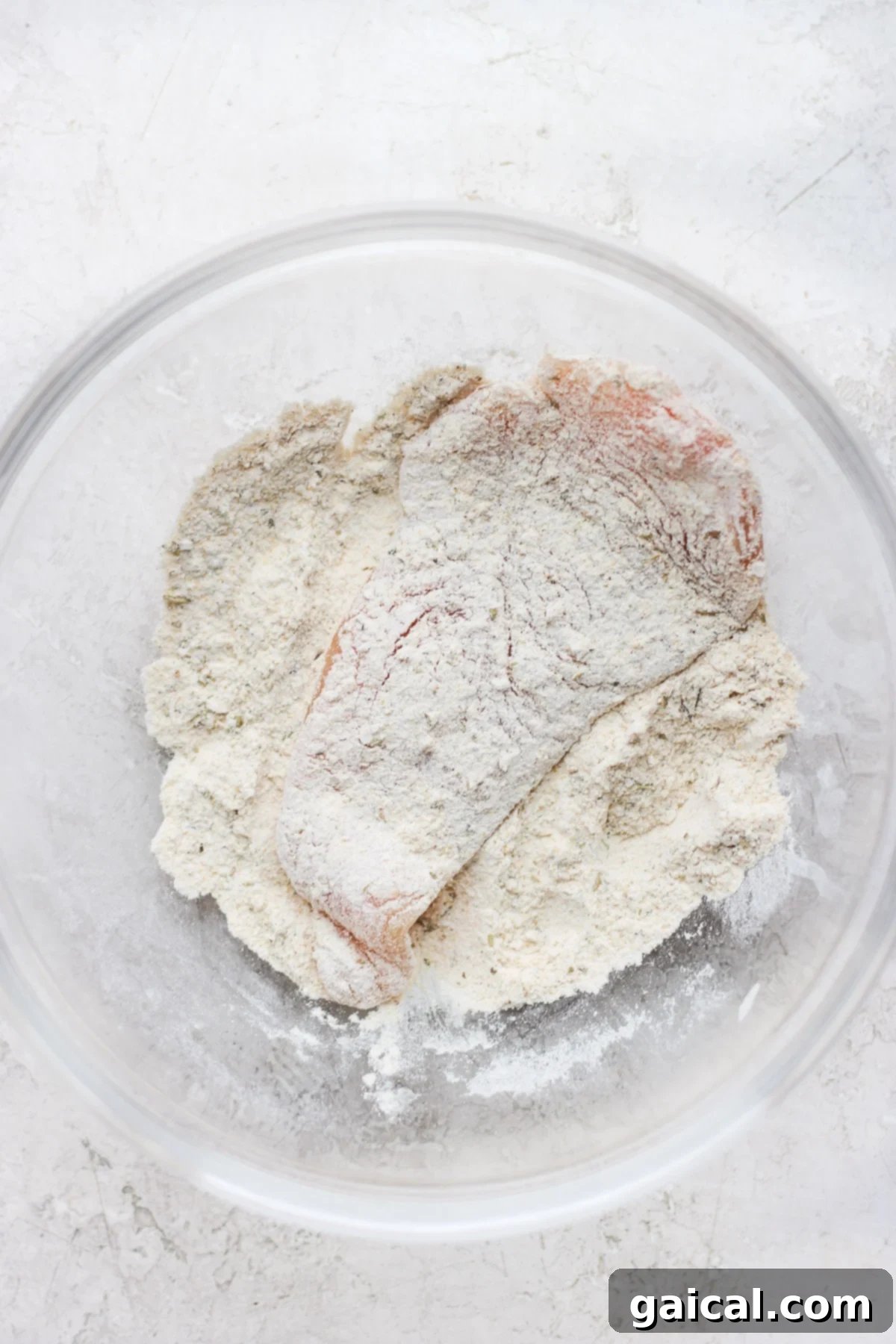 Dredging Chicken for Marsala A raw chicken breast being thoroughly coated in a flavorful seasoning and flour mixture, prepared for pan-searing to achieve a golden crust.