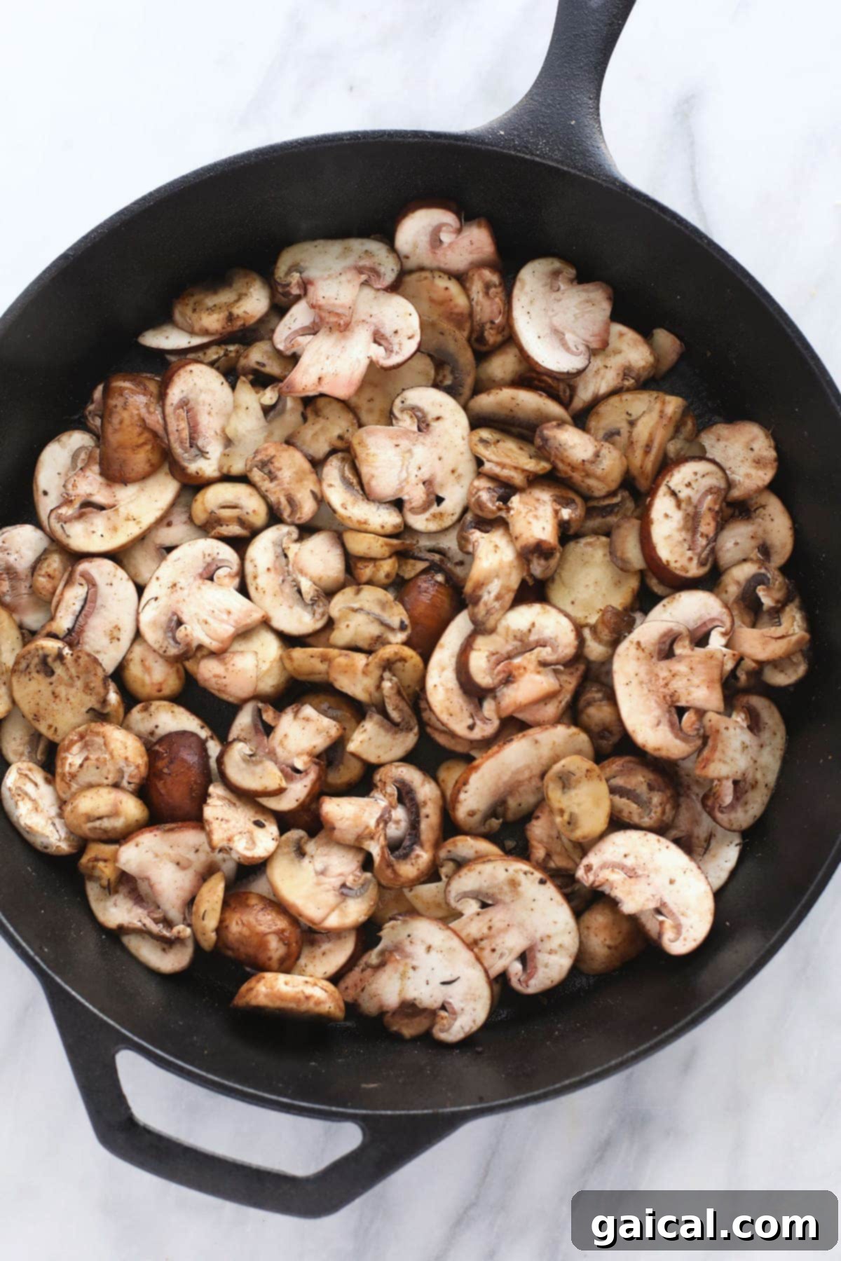 Sautéing Mushrooms for Marsala Sauce Fresh crimini mushrooms evenly spread in a hot cast iron skillet, ready to be sautéed to a deep golden brown, forming the flavorful base of the Marsala sauce.