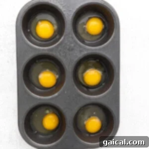 Raw eggs cracked into a greased muffin tin, seasoned and ready for the oven.