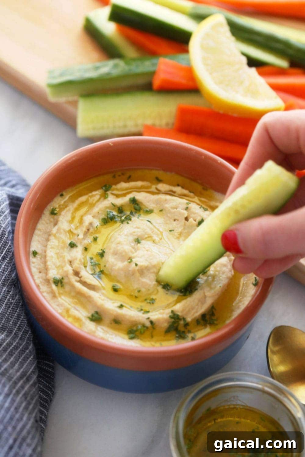 Creamy Homemade Hummus Made Easy 5 A bowl of homemade lemon garlic hummus with a fresh vegetable stick dipped into it, on a rustic wooden surface.