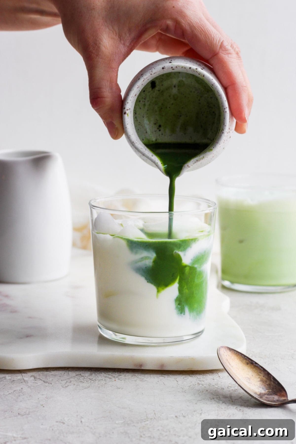 Pouring whisked matcha mixture into a glass of almond milk and ice for an iced matcha latte.