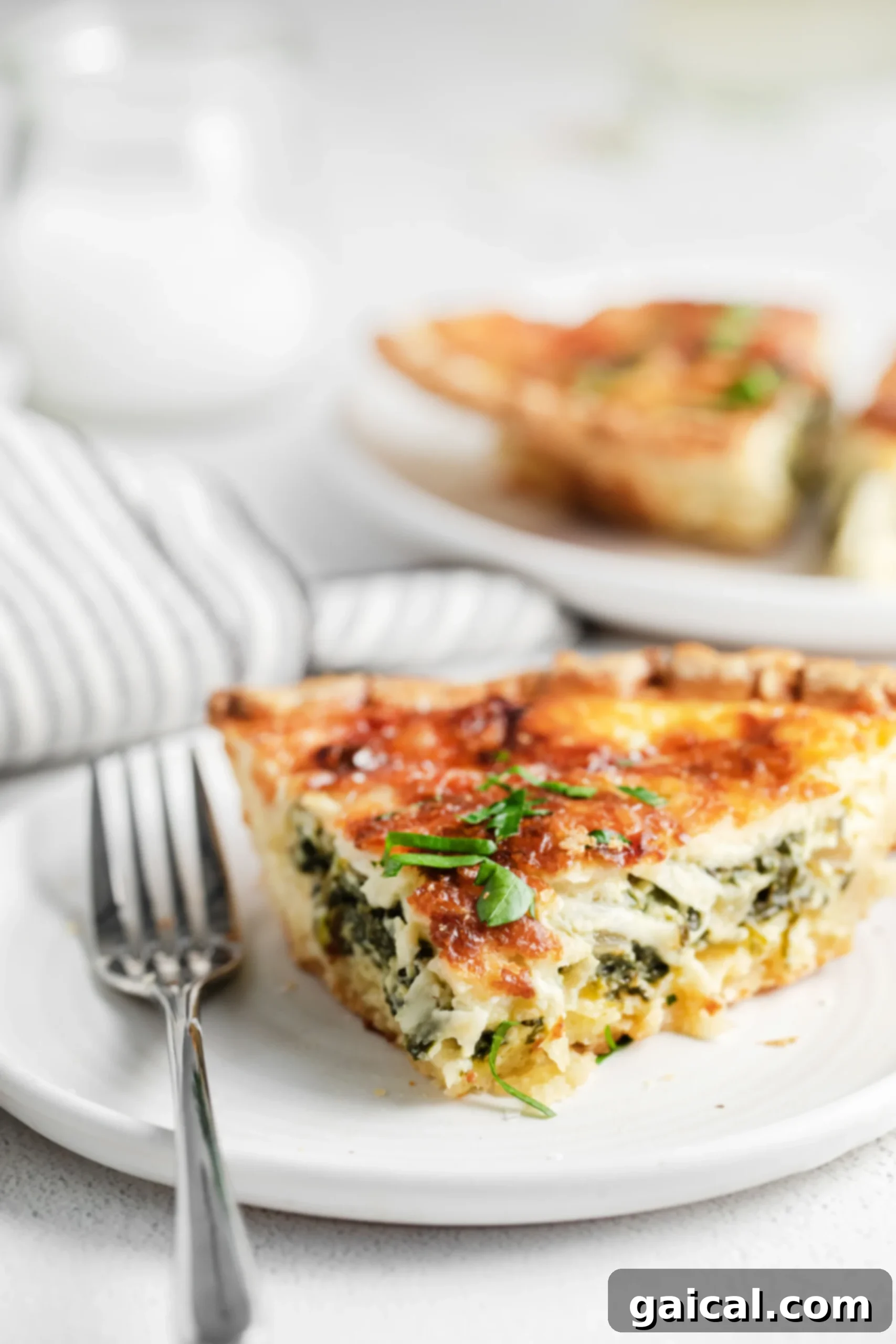 Simple & Savory Spinach Quiche 2 A perfectly baked slice of easy spinach quiche on a pristine white plate, garnished lightly, showcasing its golden crust, creamy filling, and vibrant green spinach peeking through the rich cheese topping. The setting suggests a delightful brunch or light meal.