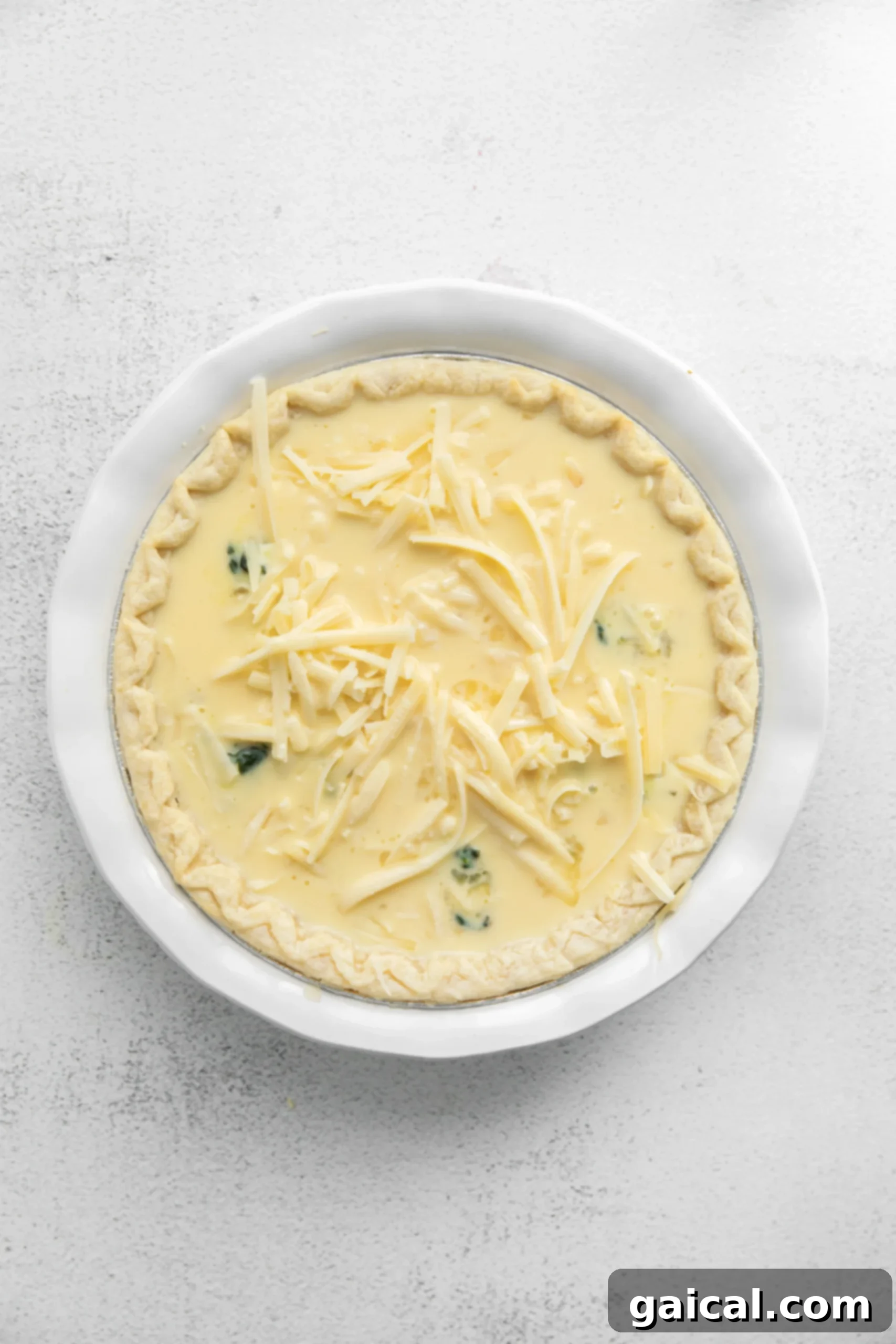 Simple & Savory Spinach Quiche 6 A baked spinach quiche, golden brown and bubbly, with a scattering of freshly grated cheese on top, ready to be served. The texture of the melted cheese and the slight browning indicates perfect doneness.
