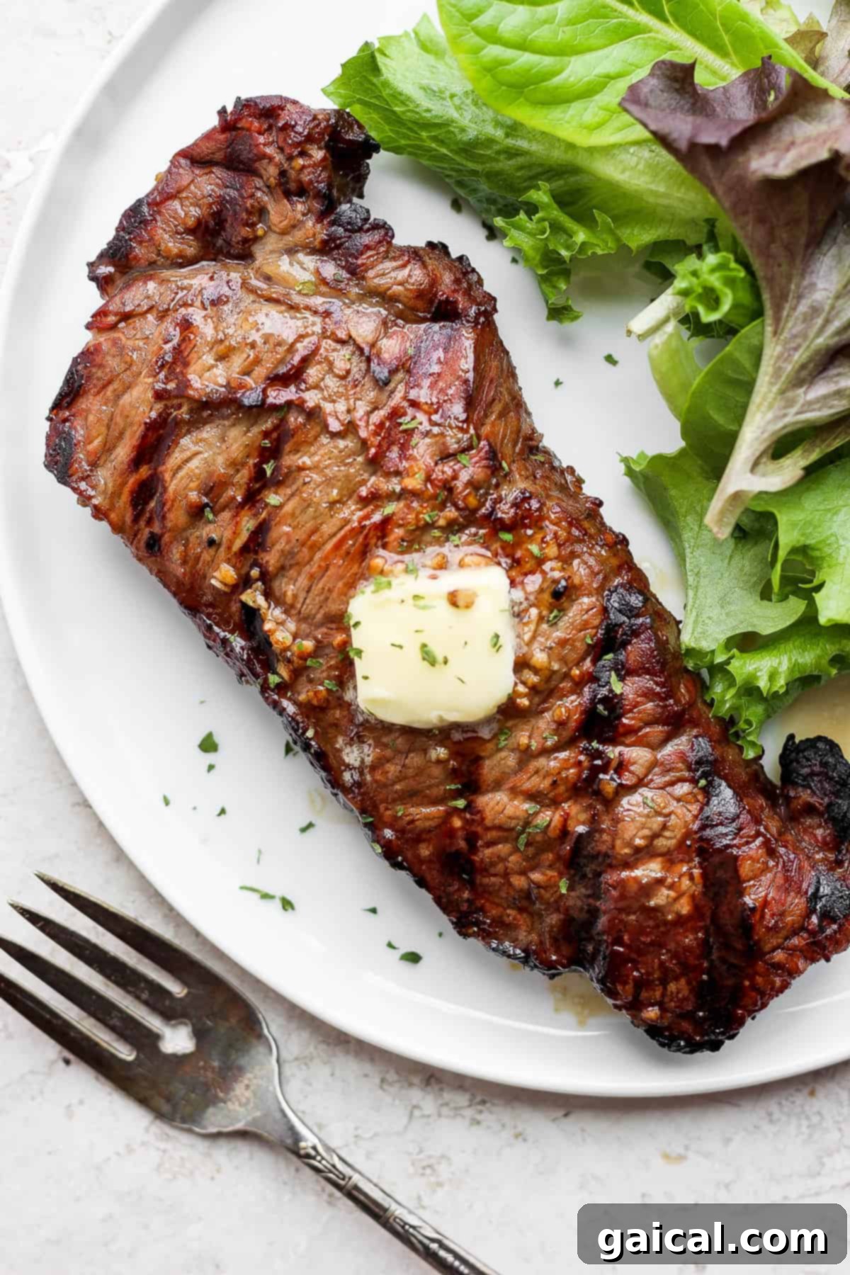 Grilled steak on a plate with melted butter, ready to be served.