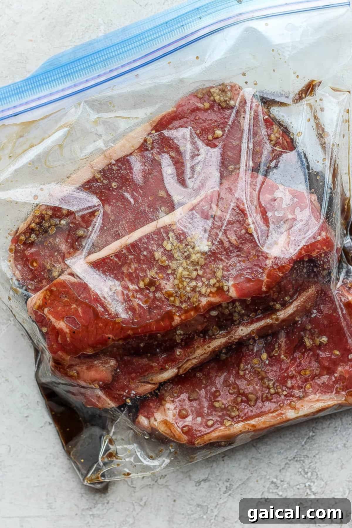 Steaks marinating in a plastic bag, coated with a rich, flavorful marinade.