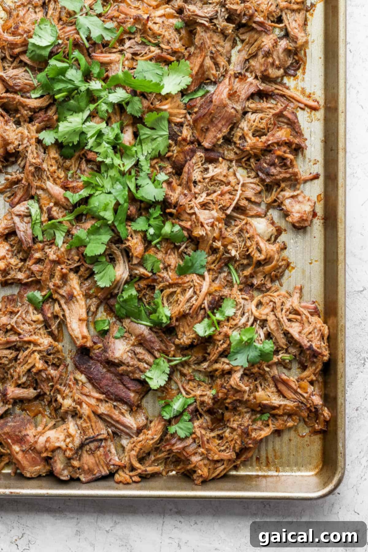This carnitas recipe sits in the slow cooker all day in delicious juices. It is shredded and crisped up in the oven for the most delicious carnitas you'll ever eat! A batch of crispy, golden-brown carnitas spread out on a baking sheet, fresh from the oven.