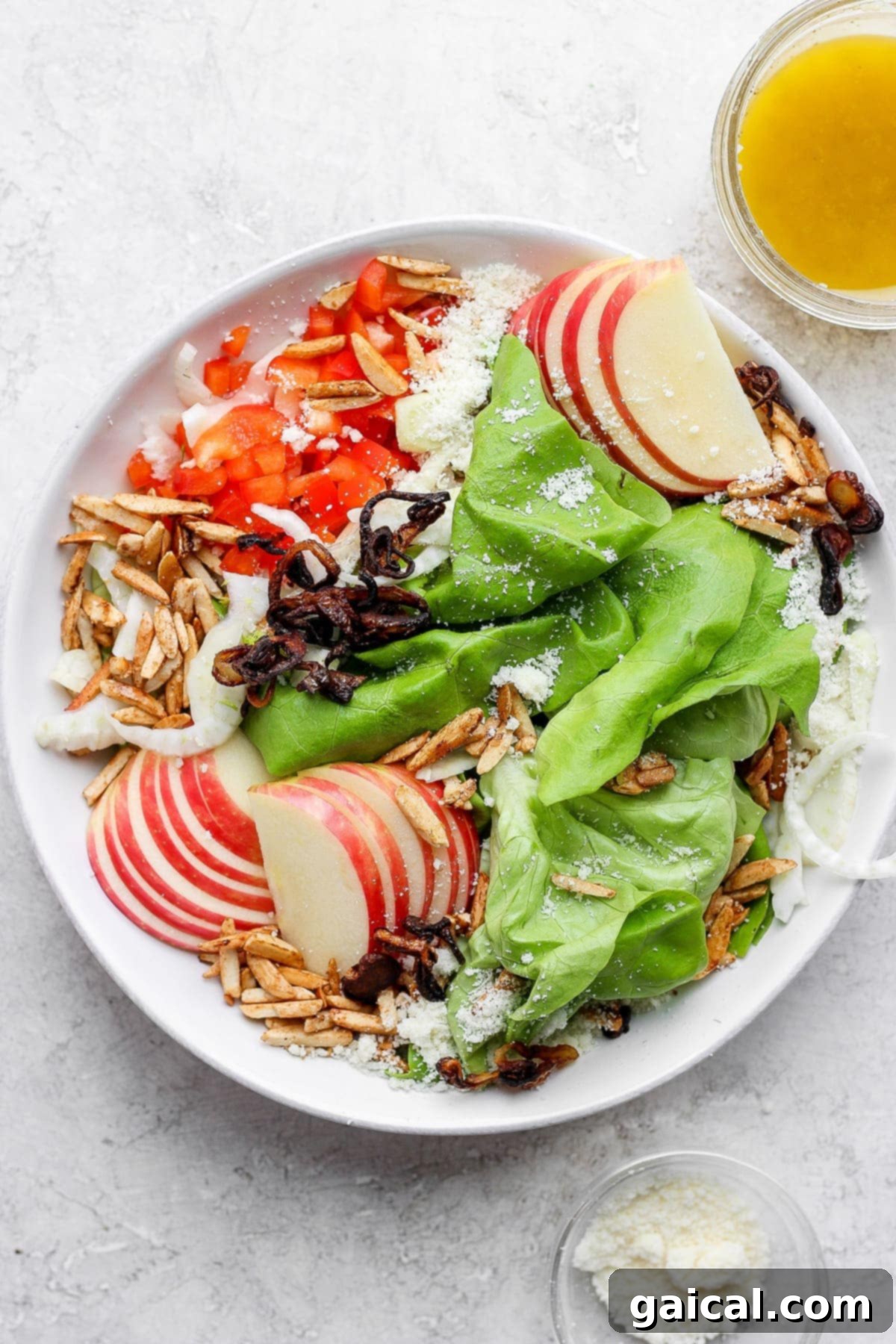 Butter lettuce salad with apples, peppers, slivered almonds, grated parmesan, and more in a salad bowl. 