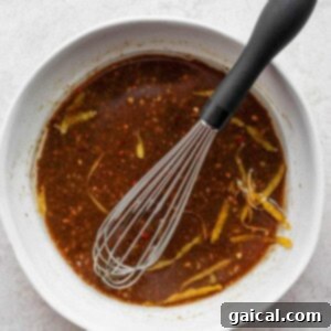 A glass bowl containing a rich, dark marinade with a whisk submerged, illustrating the mixing process for the grilled chicken marinade.