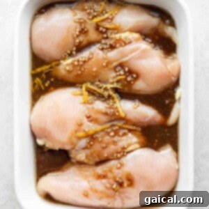 Raw chicken pieces marinating in a casserole dish, coated in a flavorful, dark liquid, preparing for grilling.