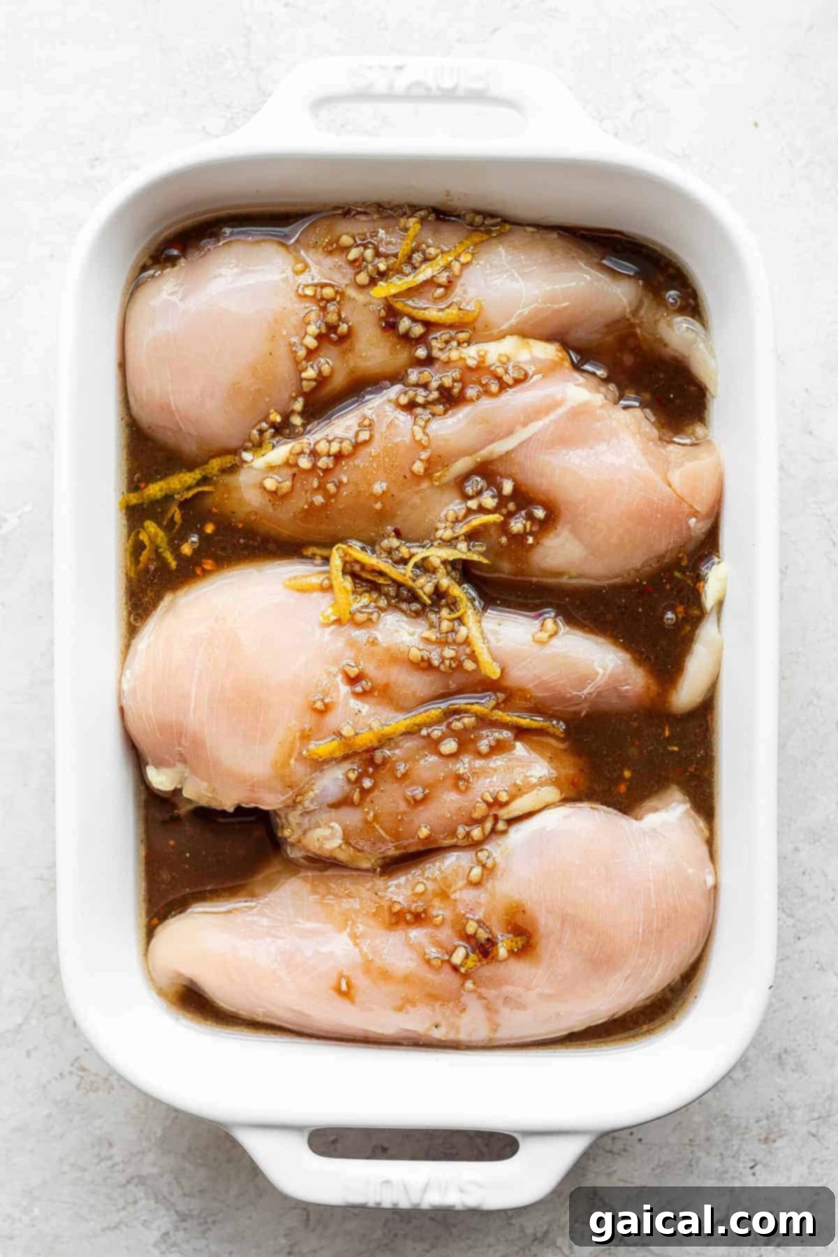 Chicken breasts soaking in the flavorful grilled chicken marinade, ready for refrigeration. Chicken breasts perfectly submerged in a rich, dark marinade within a white casserole dish, awaiting marination.
