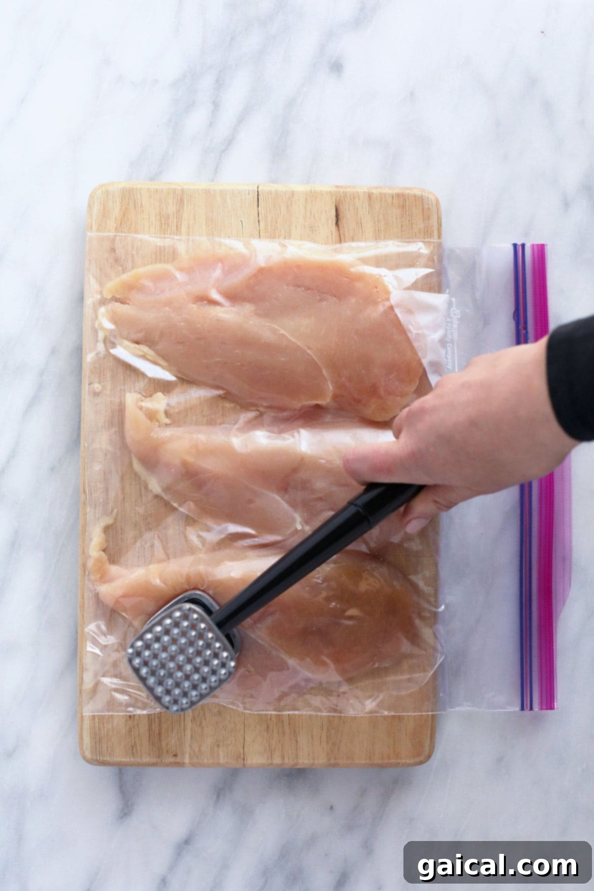 Chef tenderizing a chicken breast with a meat mallet, ensuring even thickness for cooking.