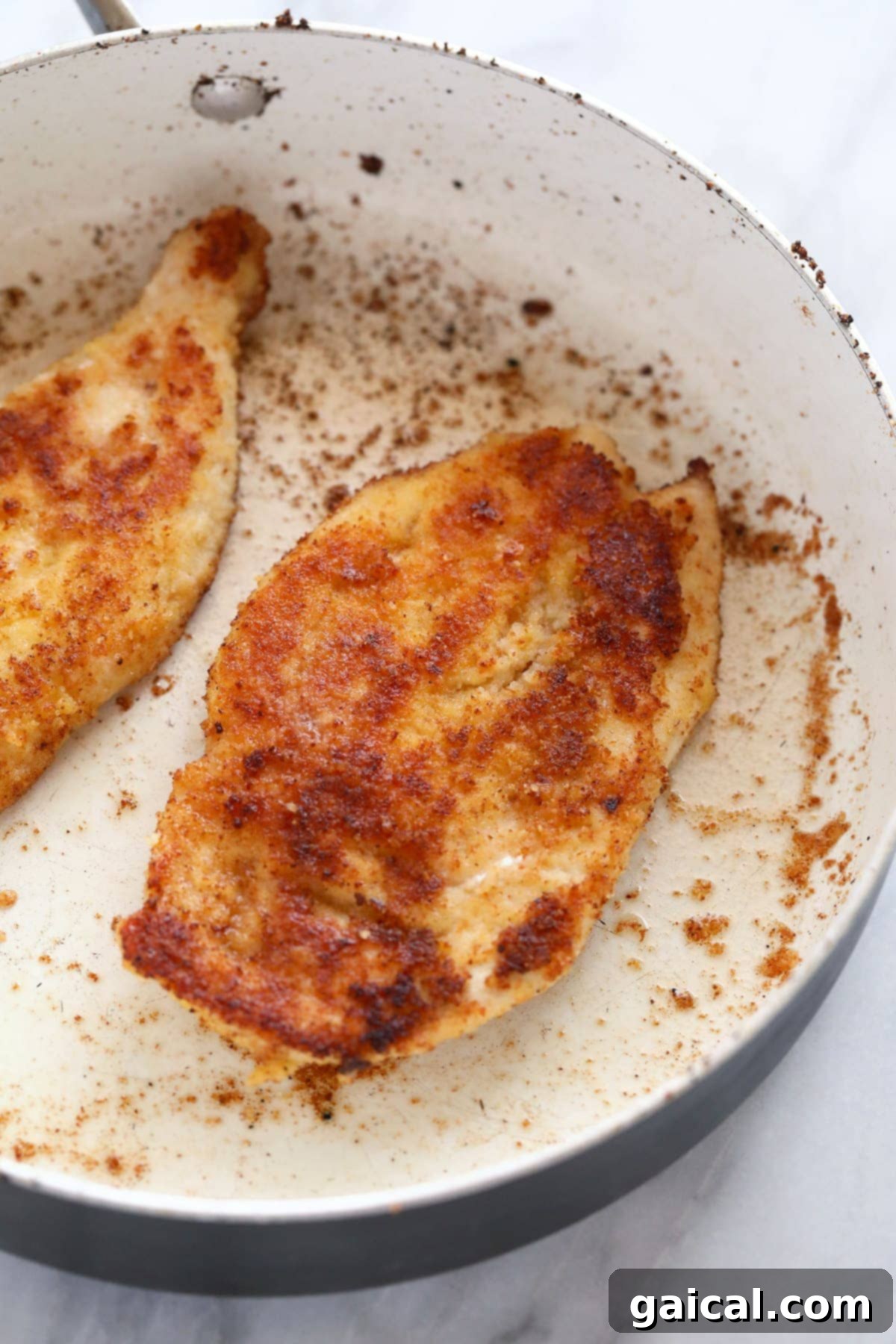Close-up view of Parmesan crusted chicken pan-frying in a skillet, showing its developing golden-brown crust.