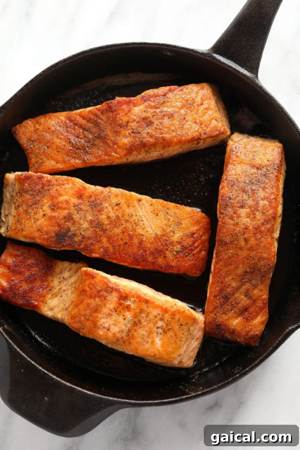 Two seared salmon fillets with crispy skin in a cast iron skillet, golden brown and ready for sauce.