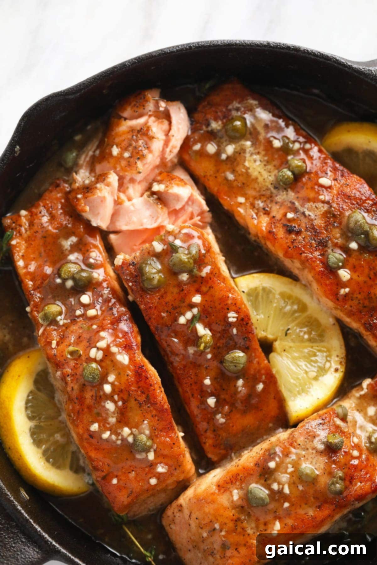 Plated salmon piccata in a cast iron pan with fresh lemons, capers, and garlic cloves, ready to be served.