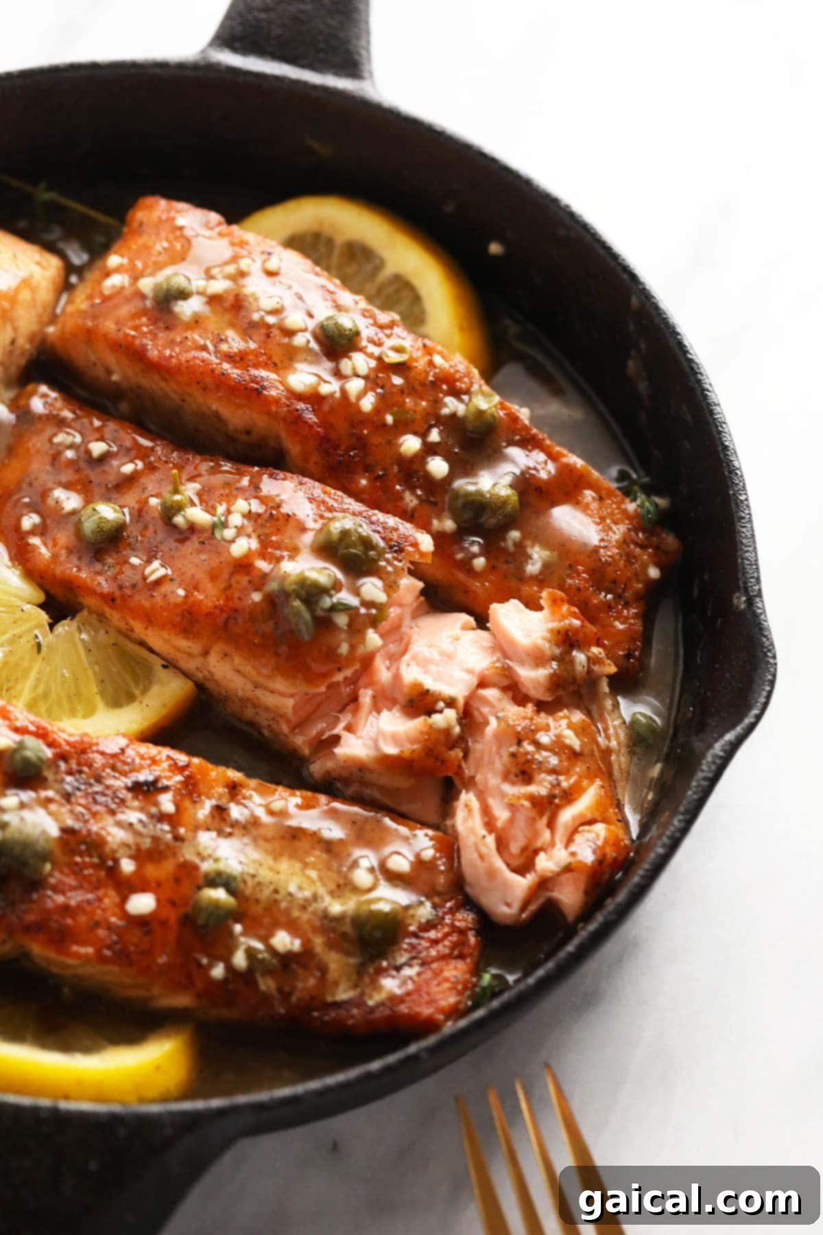 Close-up of a salmon piccata dish, highlighting the flaky salmon and the vibrant lemon-caper sauce in a cast iron pan.