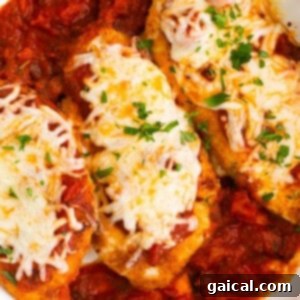 Chicken breasts in a white dish with sauce and cheese, ready for baking.