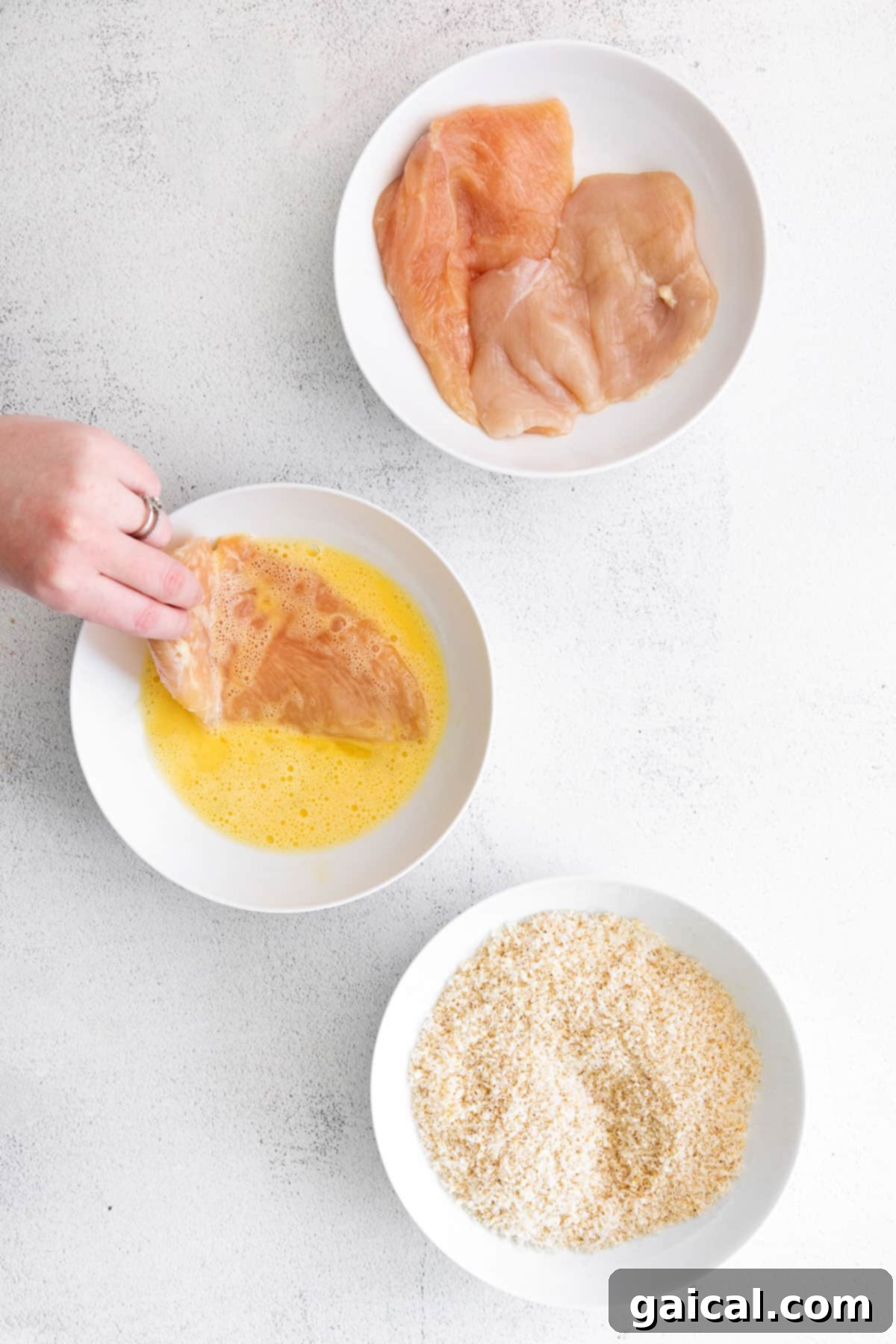 Chicken breast being dipped into an egg wash, preparing for breading.