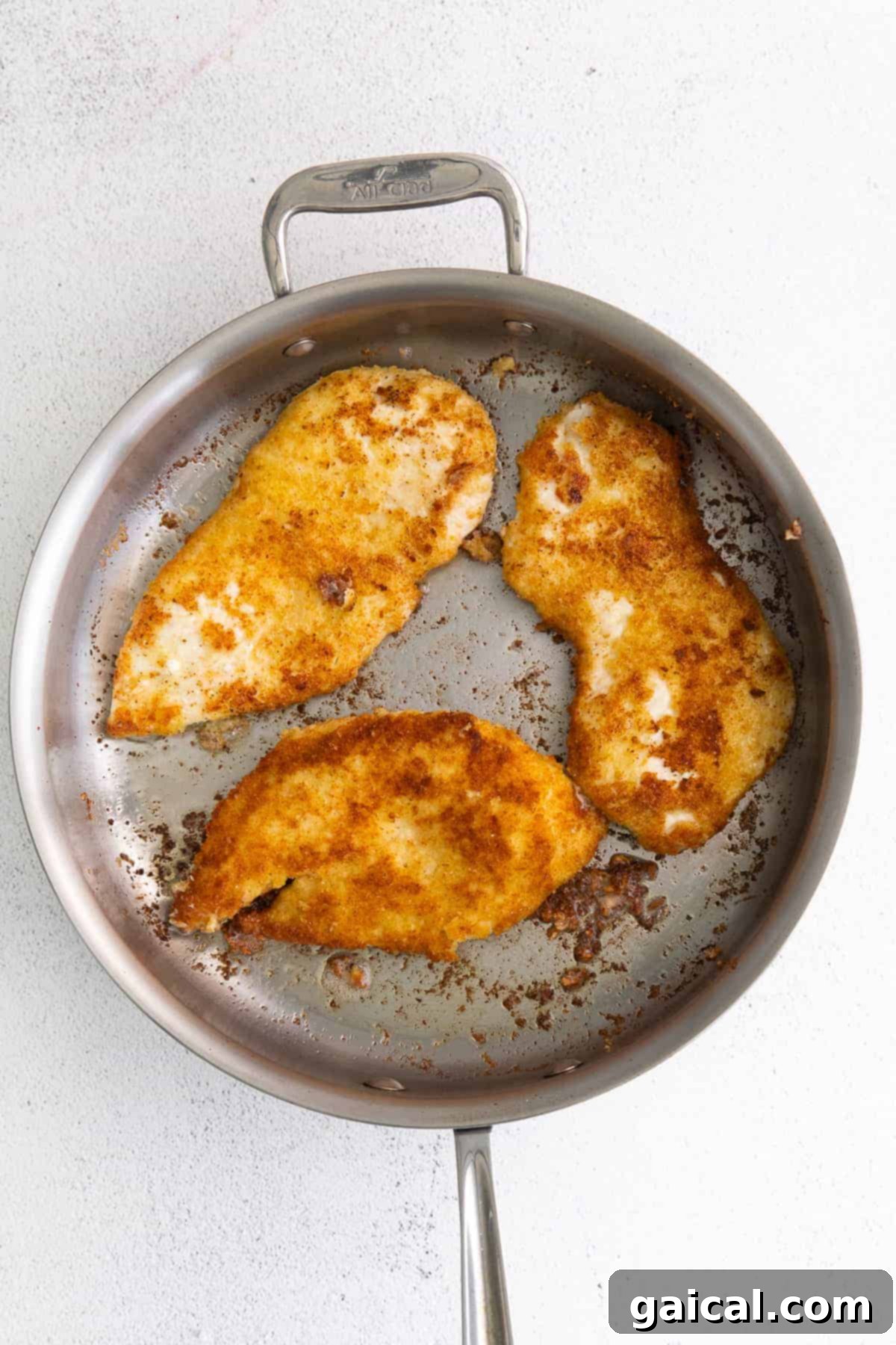 Parmesan crusted chicken cutlets pan-frying in a skillet, turning golden brown.