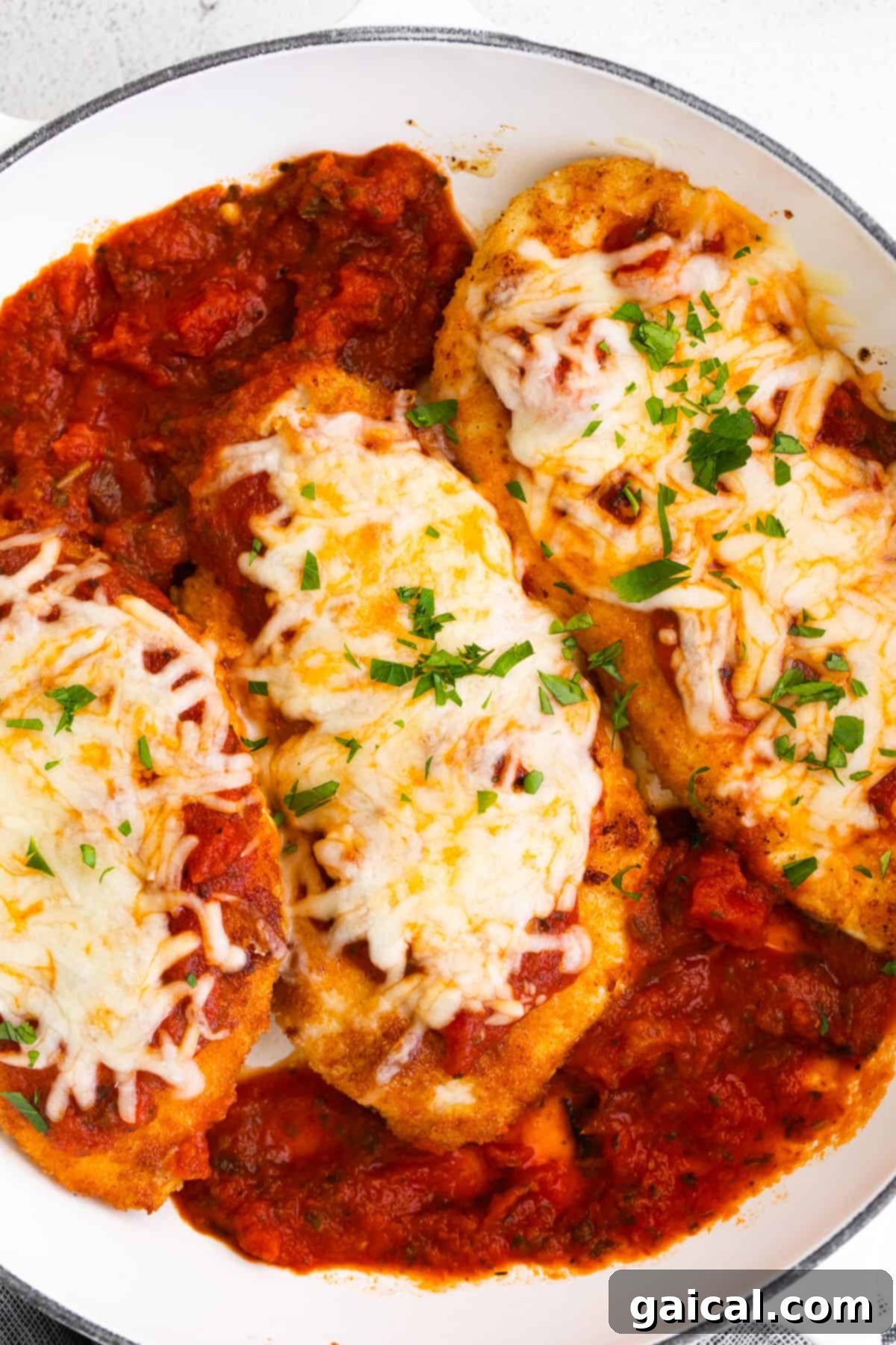 Plated chicken parmesan with cheese and fresh basil on a bed of noodles.