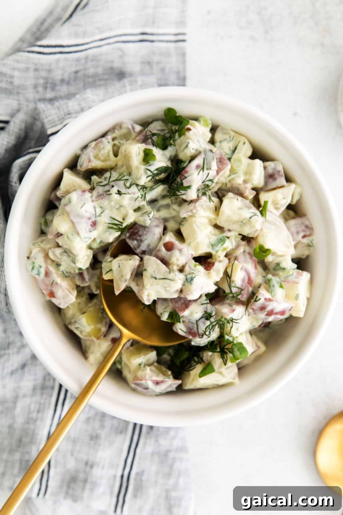 A beautifully presented bowl of creamy red potato salad, garnished with fresh dill.