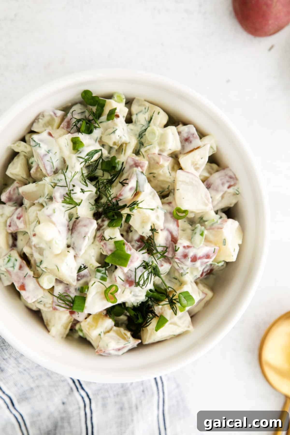 A generous serving of red potato salad in a bowl, garnished with fresh dill.
