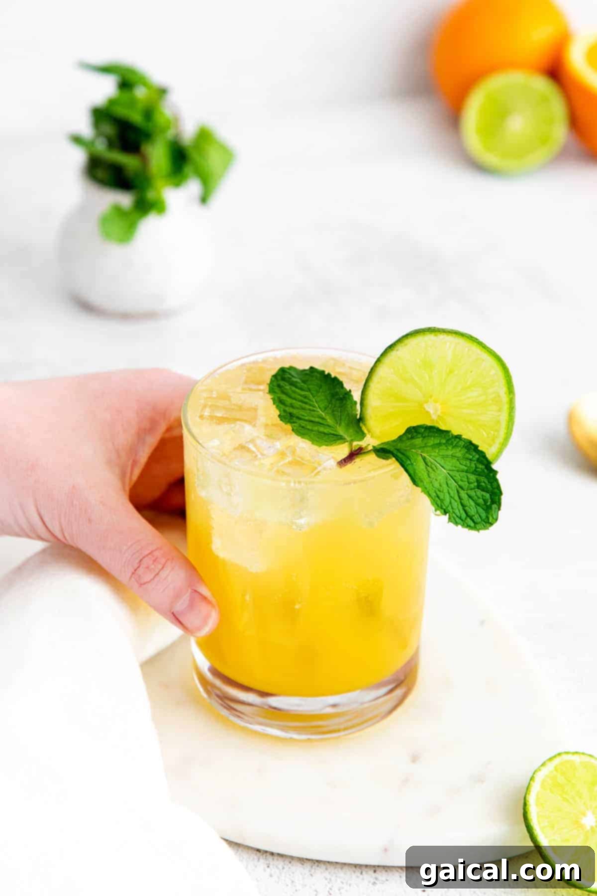 A refreshing virgin margarita, made with lime juice, agave nectar, orange juice, and sparkling water. Hand holding a refreshing virgin margarita, garnished with a lime wedge.