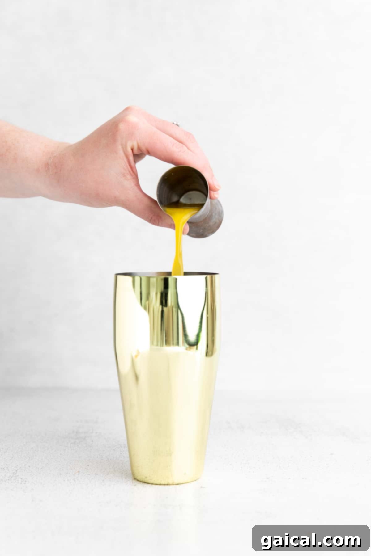 Preparing the base for a refreshing virgin margarita in a cocktail shaker. Pouring fresh orange juice into a cocktail shaker, alongside lime juice and agave nectar.