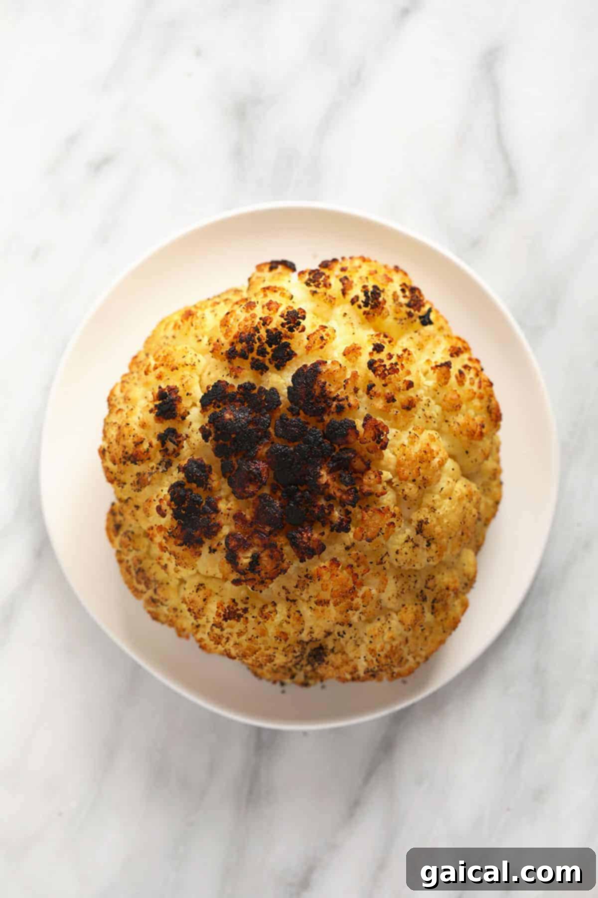 Fire-Kissed Cauliflower 5 A stunning shot of grilled cauliflower on a pristine white plate, adorned with herbs, highlighting its crispy texture and golden-brown char.