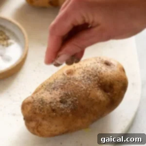 Smoke-Kissed Baked Potatoes 3 a person is sprinkling salt on some potatoes.