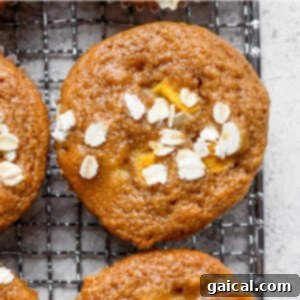 A cooling rack with freshly baked peach muffins, some adorned with almonds, ready to be enjoyed.