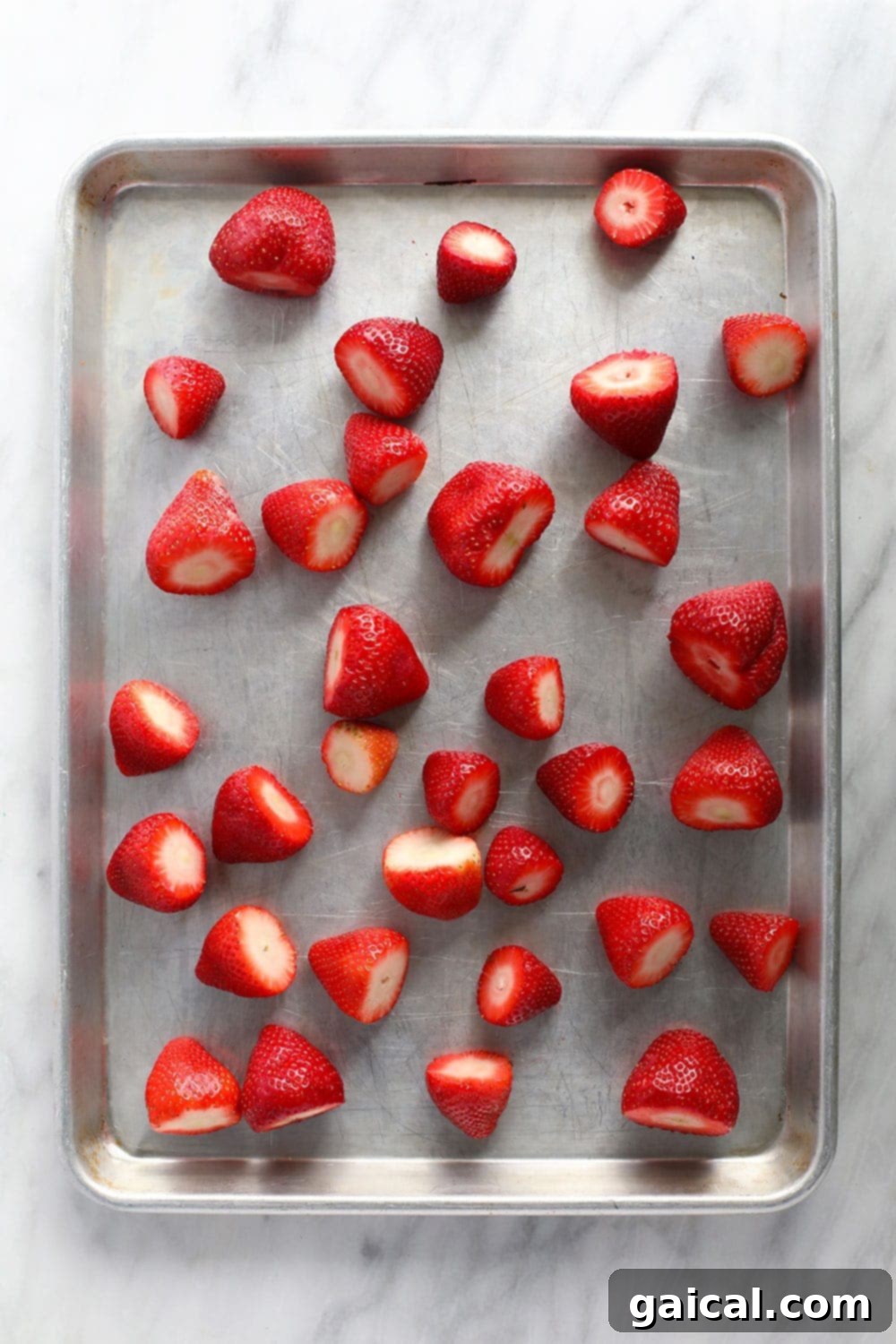 Whole strawberries spread out evenly in a single layer on a parchment-lined baking sheet for flash freezing, prior to storage.