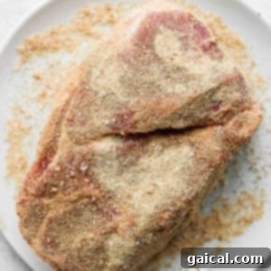 A boneless pork shoulder roast generously coated with a savory dry rub, ready for searing.