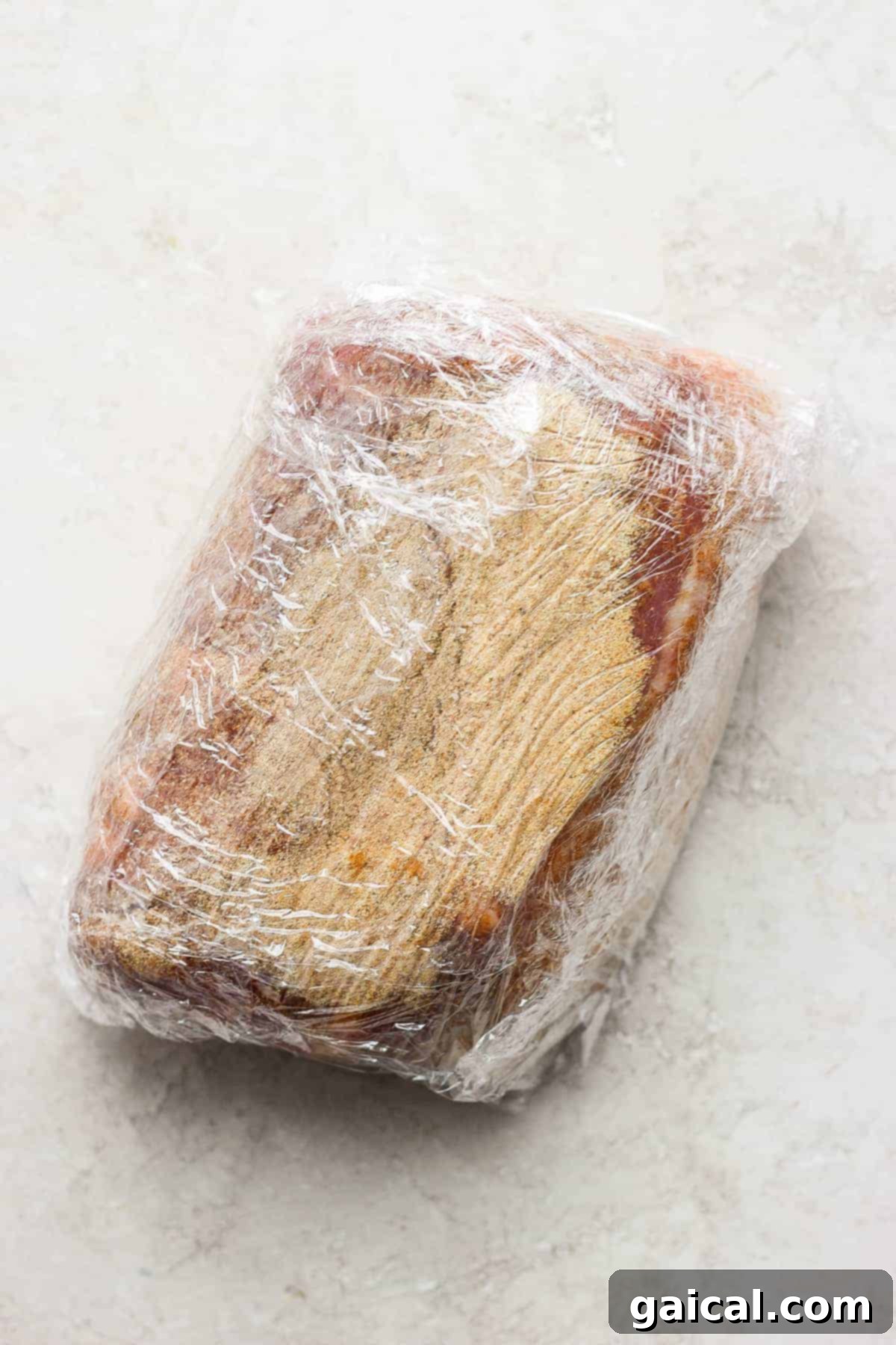 Pork shoulder wrapped tightly in plastic wrap, indicating preparation for an overnight dry rub marination in the fridge.