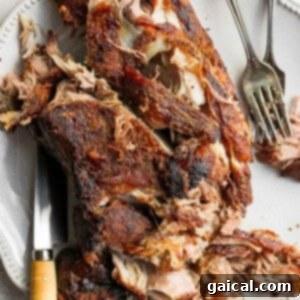 Slow Roasted Pork Shoulder on a serving plate, highlighting its crispy crust and tender, shredded texture.