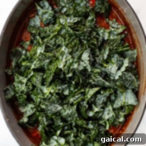 Hearty Quinoa Chili 7 Fresh kale being stirred into the simmering quinoa chili in a pot.