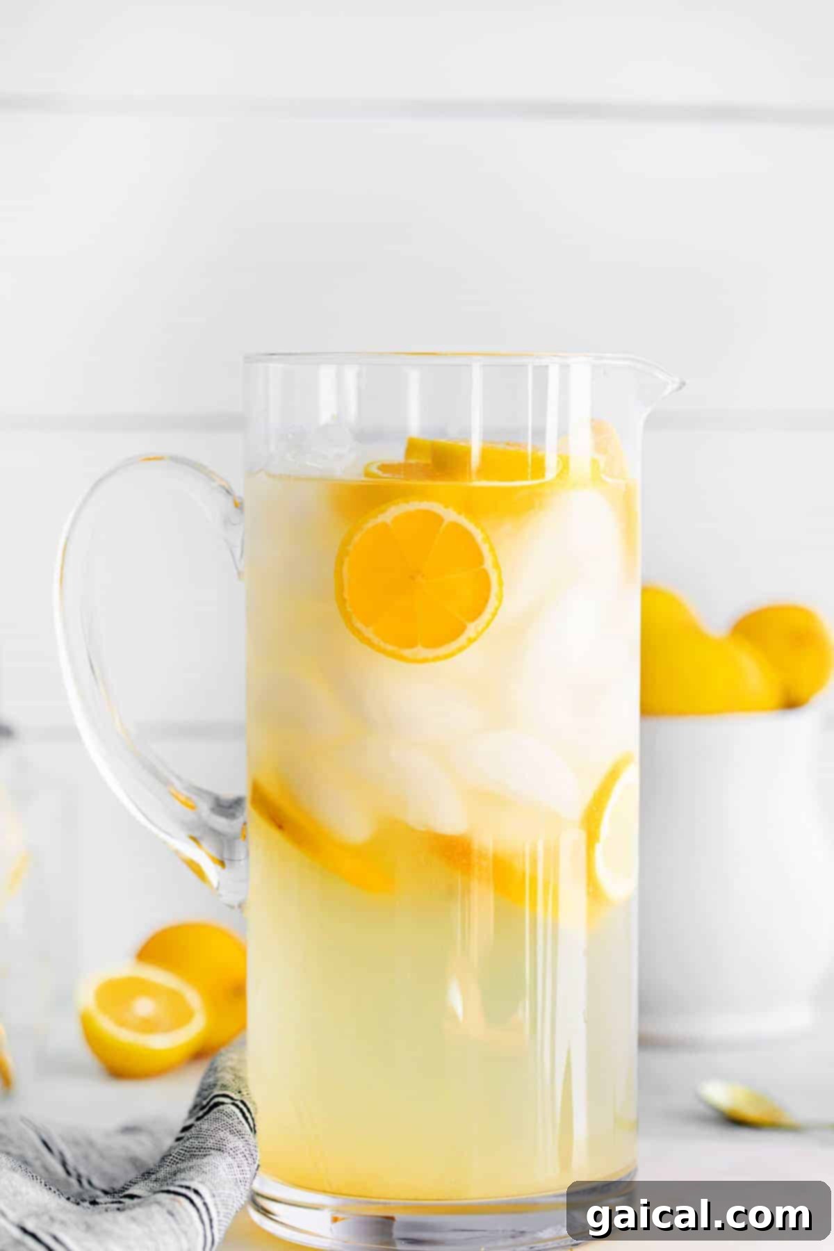 A large glass pitcher of homemade lemonade, brimming with ice and vibrant lemon slices, chilling on a countertop.