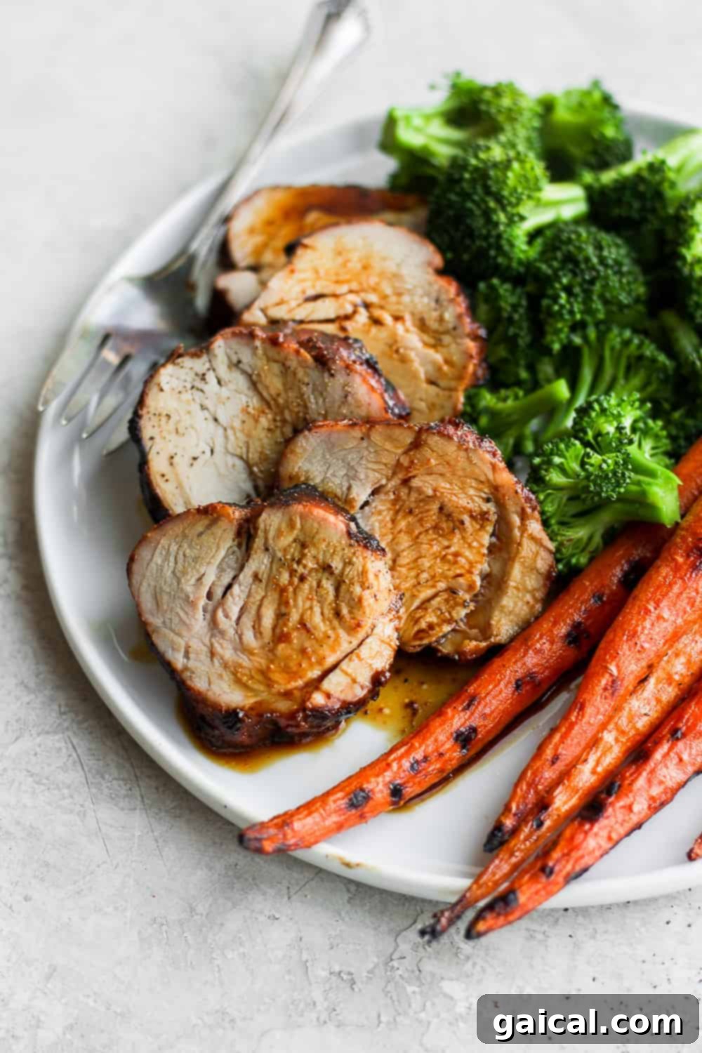 Juicy, perfectly sliced pork tenderloin on a clean white plate, ready to serve with a garnish.