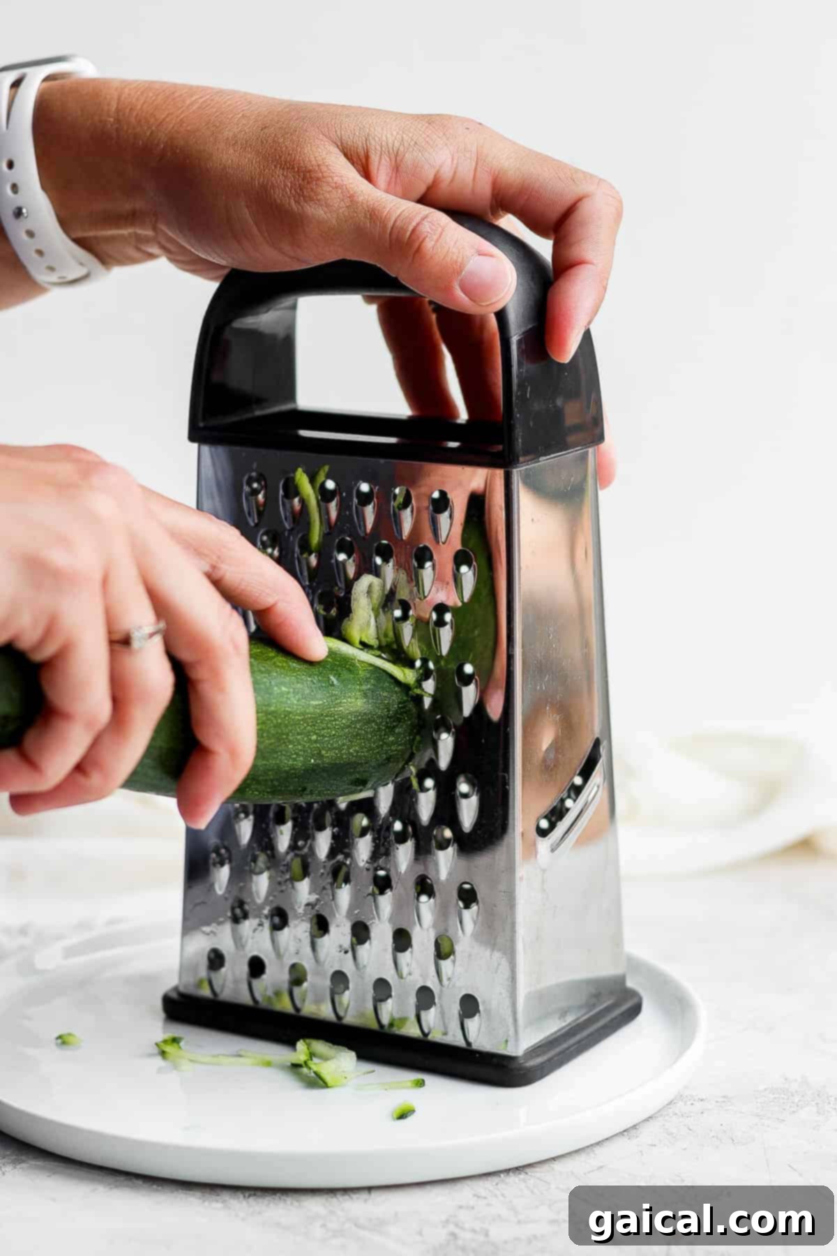 Preparing grated zucchini for oatmeal cookies. Hands grating fresh zucchini with a box grater.