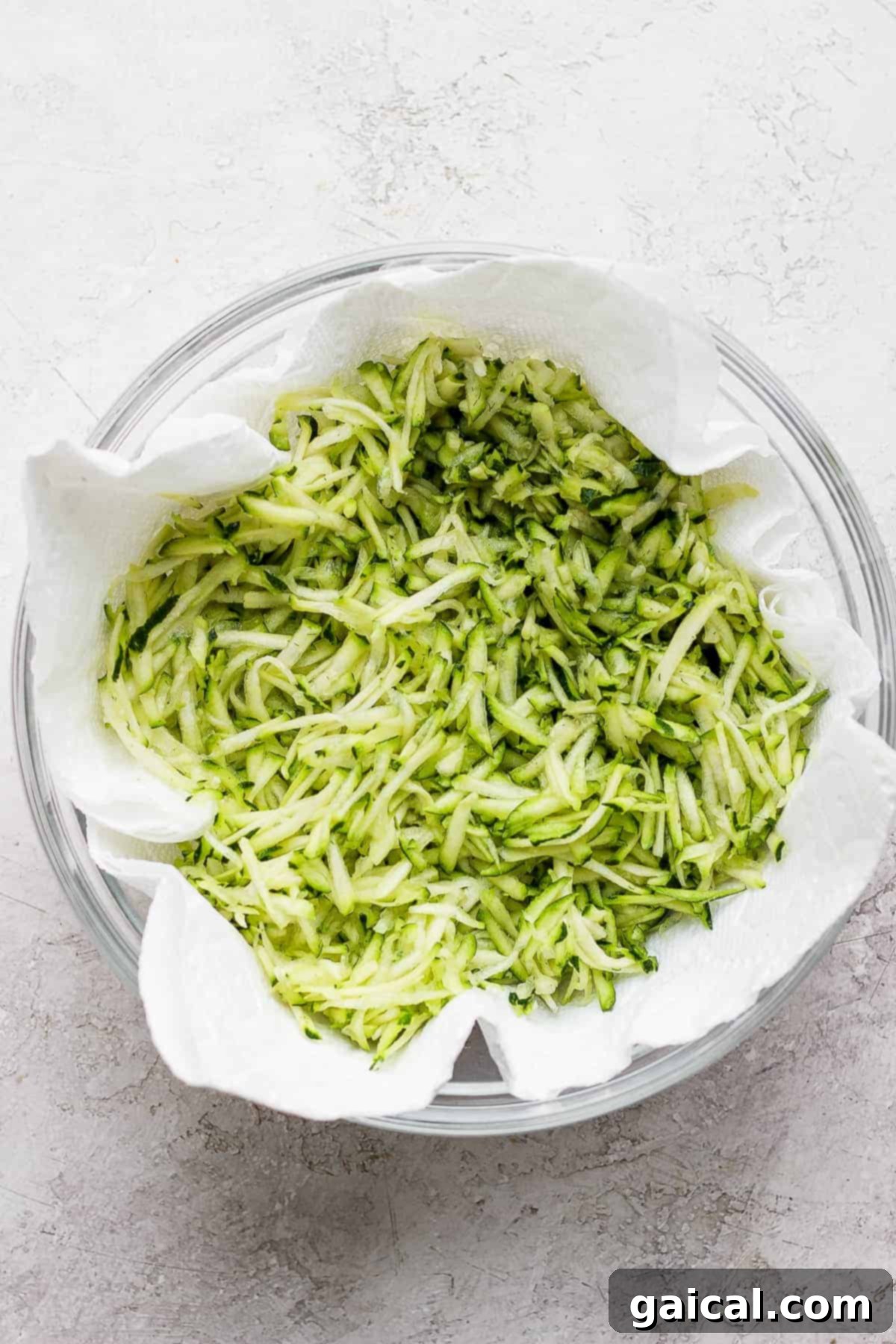 Shredded zucchini ready for moisture removal. A bowl filled with freshly shredded zucchini, waiting to be blotted.