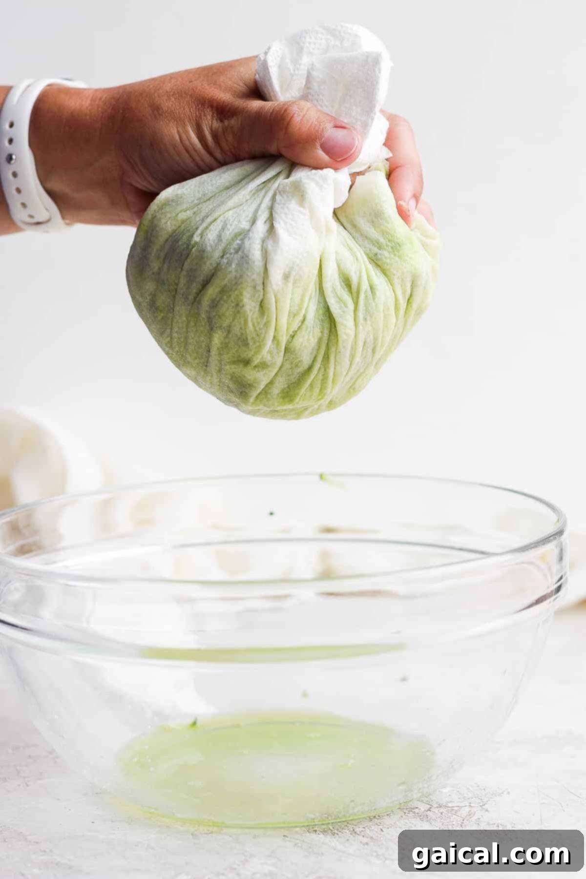 The essential step of squeezing liquid from zucchini. Hands squeezing excess moisture from grated zucchini using a tea towel.
