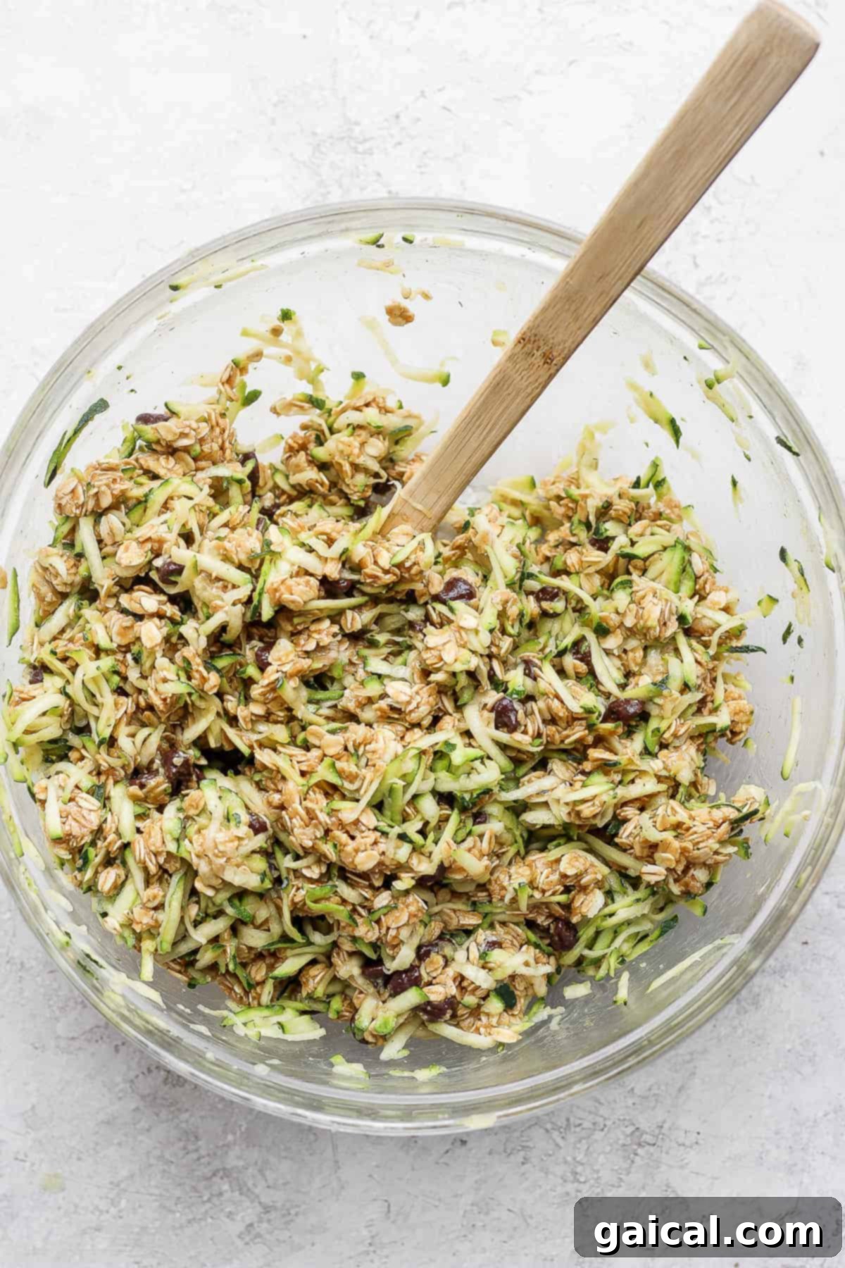 Zucchini oatmeal cookie dough in a mixing bowl. Bowl of freshly prepared oatmeal cookie batter with shredded zucchini and chocolate chips.